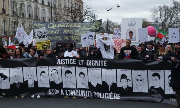 A photograph of the March for Dignity in Paris. Marchers are holding up a placard that reads 'Justice and Dignity' and 'Stop Police Violence'
